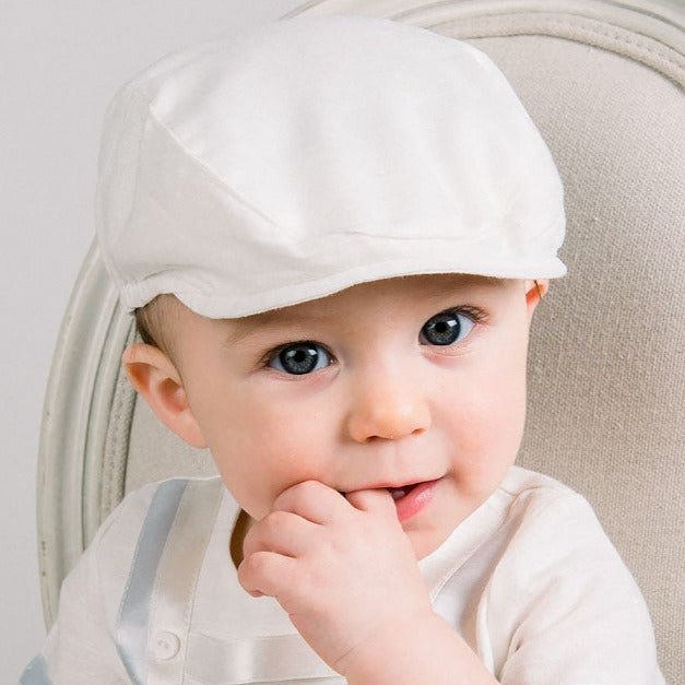 Baby boy wearing a Oliver Linen Newsboy Cap in white. It is made linen cotton blend and features a soft elastic band around the back.