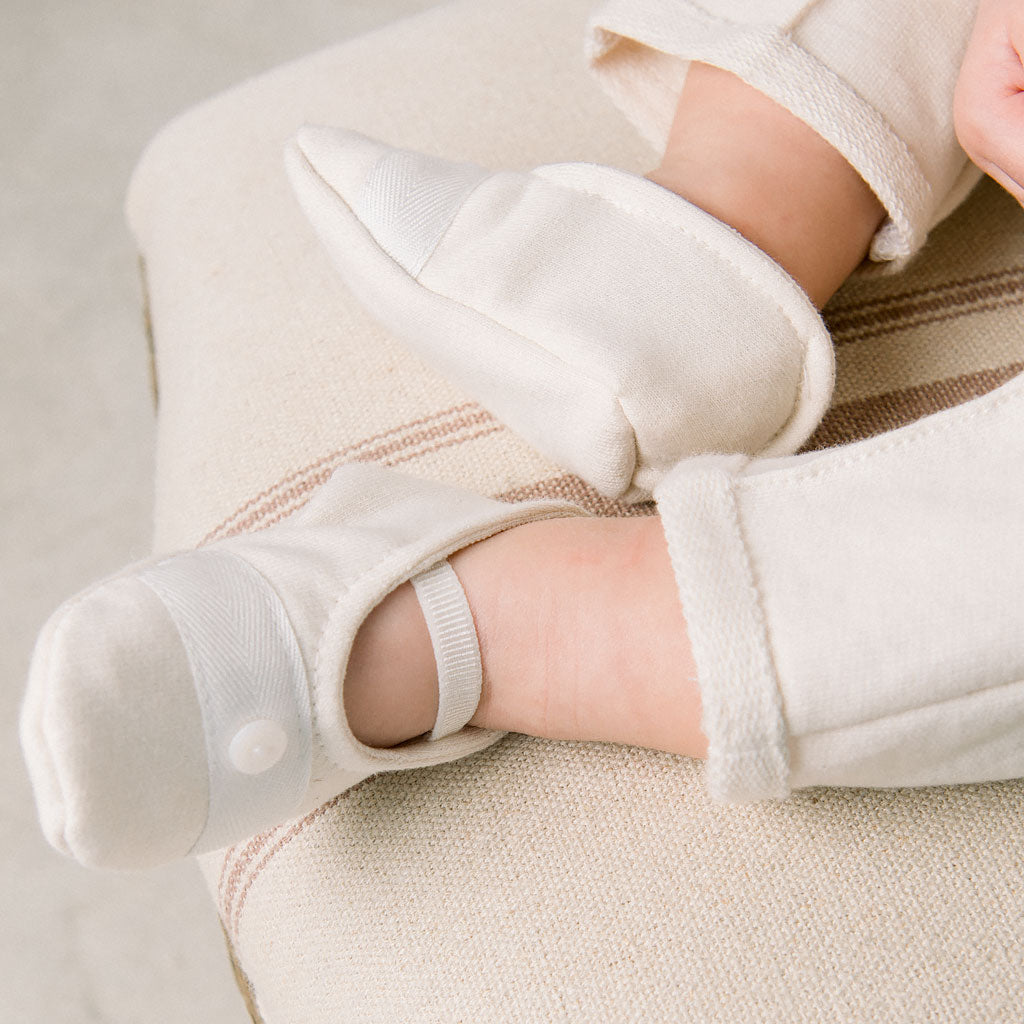 Baby wearing the Miles Booties made from ivory french terry cotton and featuring a grosgrain ribbon detailing with a button