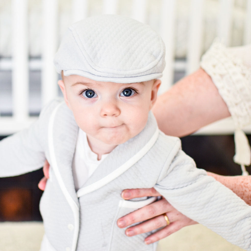 Baby boy smiling in his newsboy cap and the gray asher baptism suit. 