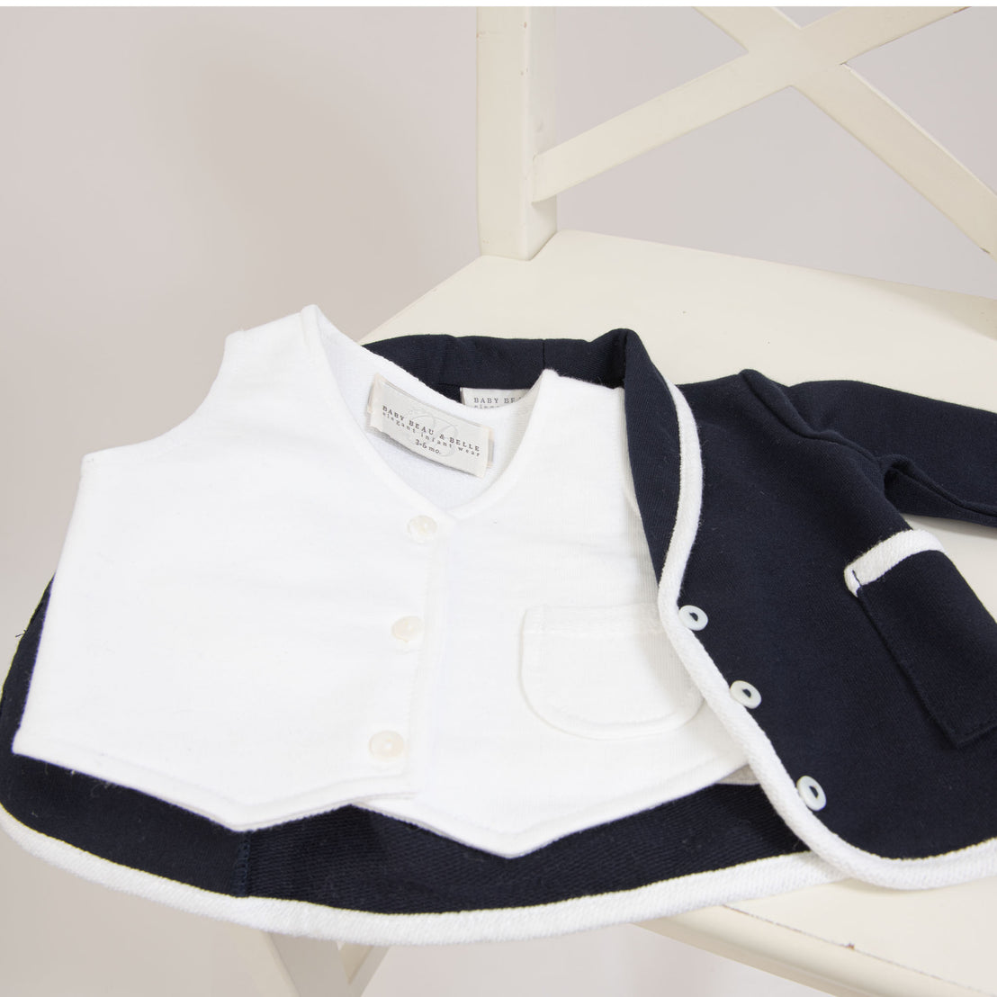 Flat lay photo of the Elliott Vest, made with a white French Terry Cotton with a three button closure and darling pocket detail, paired with the Elliott Jacket.