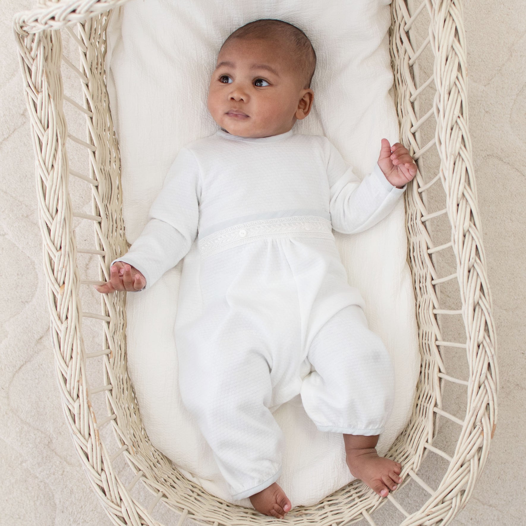 Infant dressed in the Harrison Long Sleeve Christening Romper, lying peacefully in a basket with intricate lacework and soft white design.