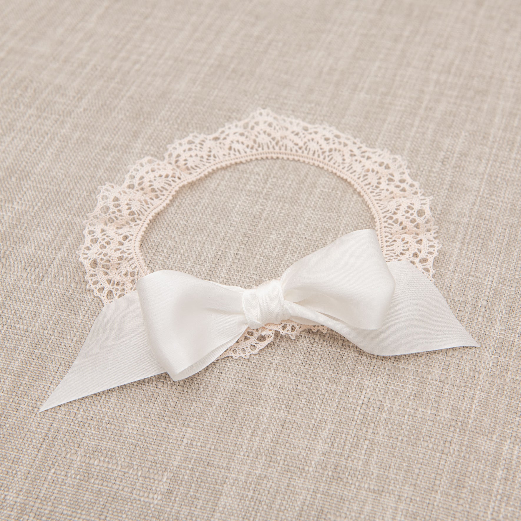 Flat lay photo of the Tessa Lace Headband, which is made with from an elastic lace in Vintage Pink and finished with an Ivory silk ribbon bow.