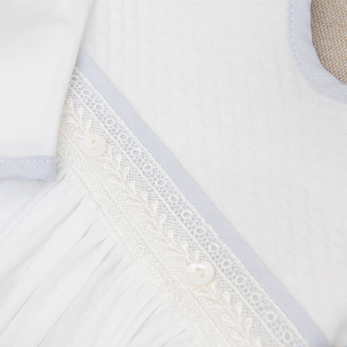 Close up detail of the Harrison Newborn Gown featuring the ivory Venice lace accent along the bodice and light blue linen trim 