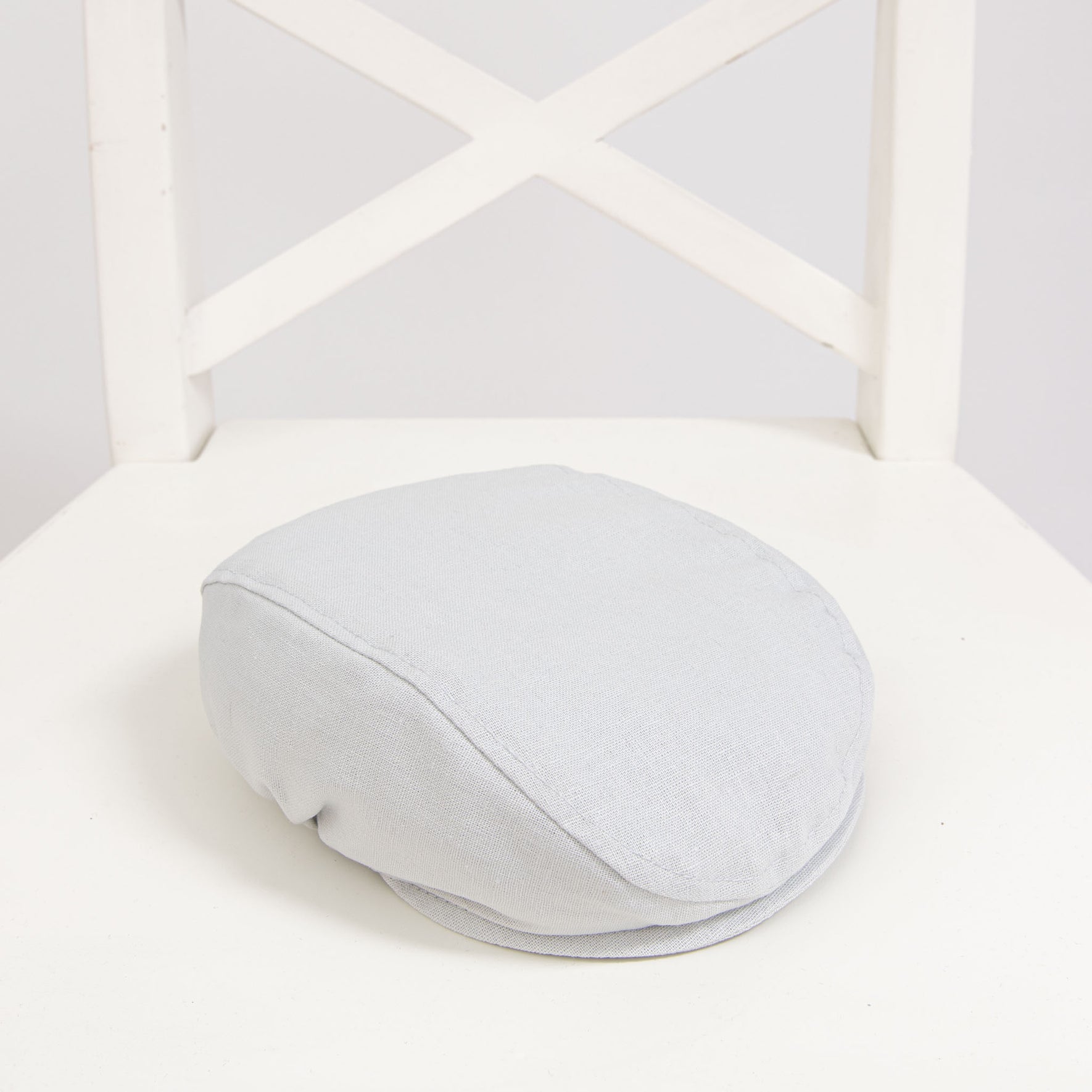Flat lay photo of the Grayson Linen Newsboy Cap. The hat is made from a linen/cotton blend in grey with a soft elastic band around the back.