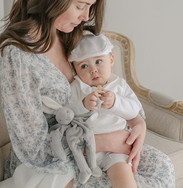 Baby boy with his mother. He is holding onto the Miles Silly Bunny Pacifier Holder, a grey bunny stuffed animal