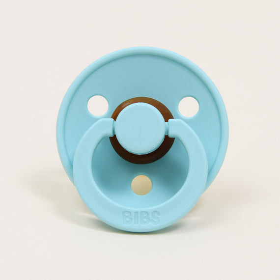 A mint pacifier with a circular shield featuring two holes, crafted from natural rubber to aid in soothing babies. The handle is embossed with the brand name "Bibs," which is renowned for its design and manufacturing in Denmark.