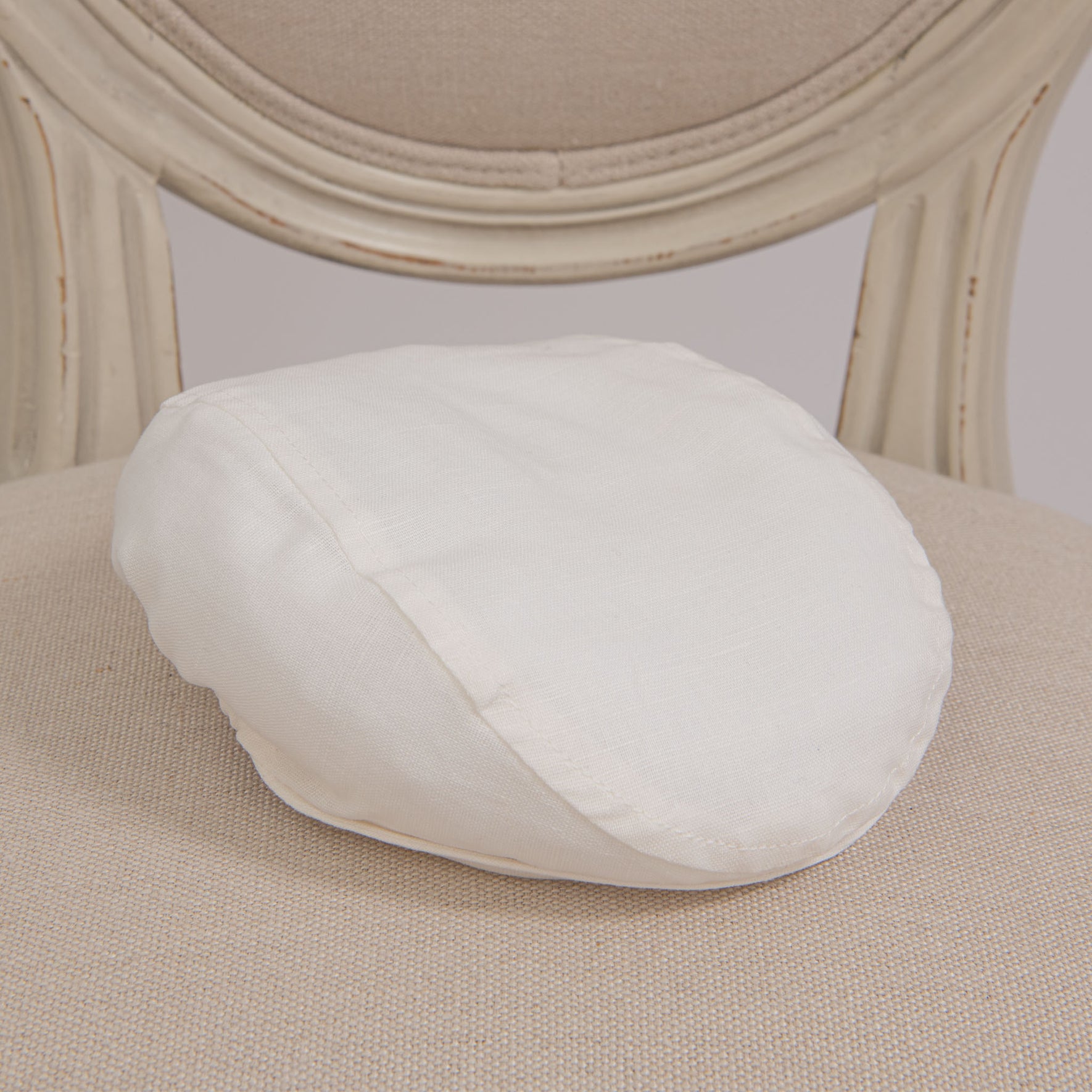 Flat lay photo of the Owen Linen Newsboy Cap on a chair. The hat is made from a Linen/cotton blend in light ivory