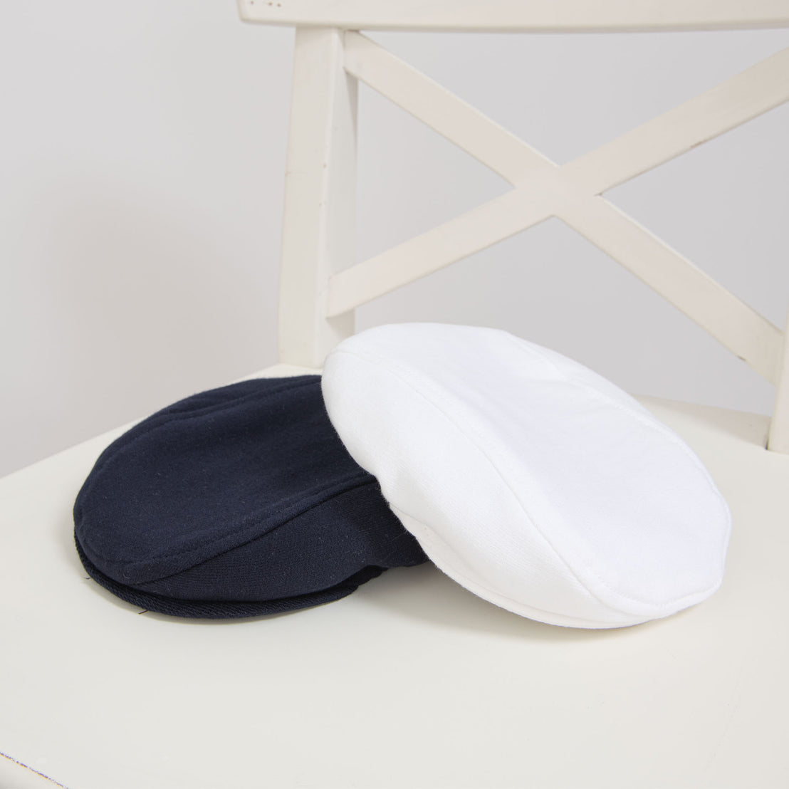 Flat lay photo of the Elliott Newsboy Caps: one in navy and the other in white french terry cotton.
