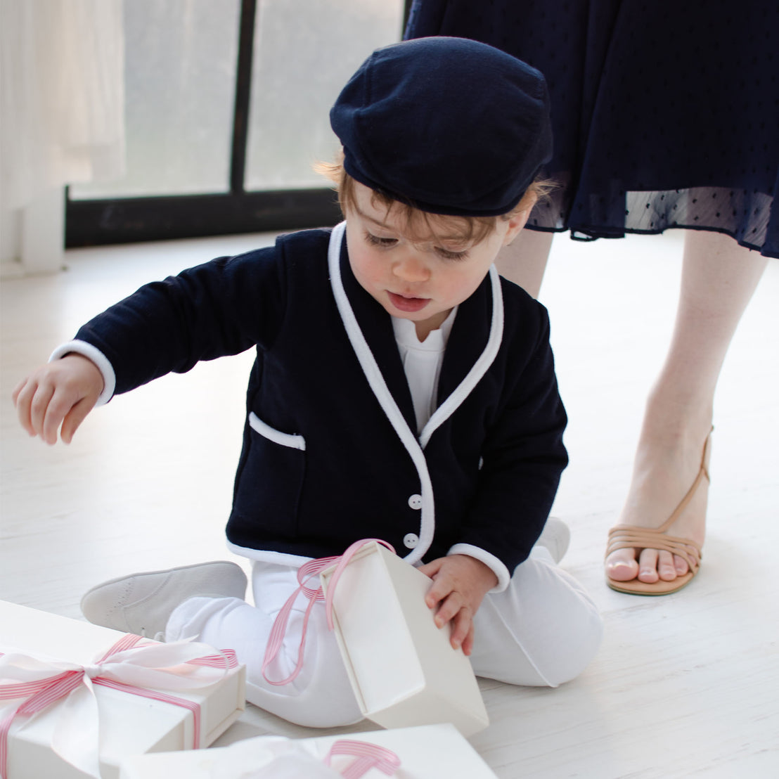 Baby boy playing with gift boxes.  He is wearing the Elliott 3-Piece Suit, including jacket, pants, and onesie (and matching navy newsboy cap).