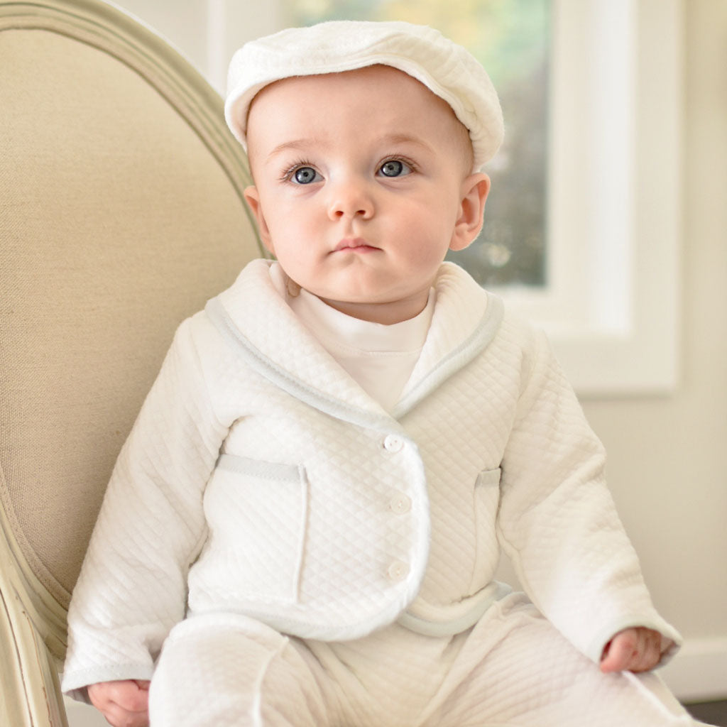 Baby boy sitting on a chair wearing the Harrison 3-Piece Pants Suit made with plush white quilted cotton jack, pants, and hat