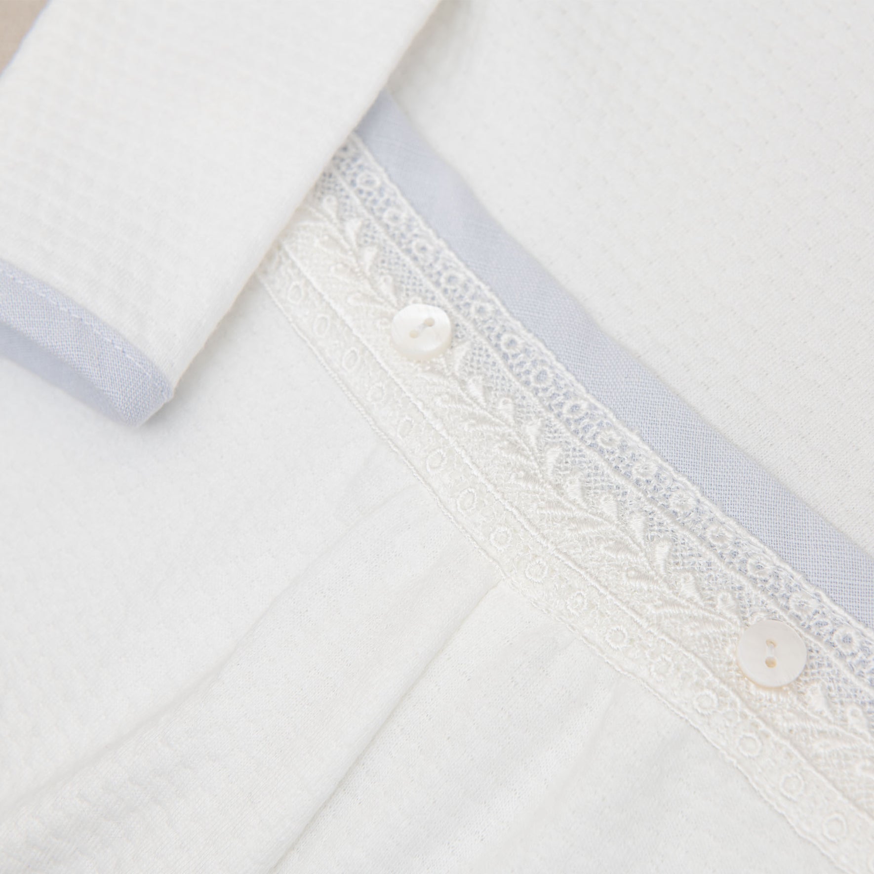 Detailed view of the Harrison Long Sleeve Christening Romper's waistband, featuring delicate lace accents and button details.
