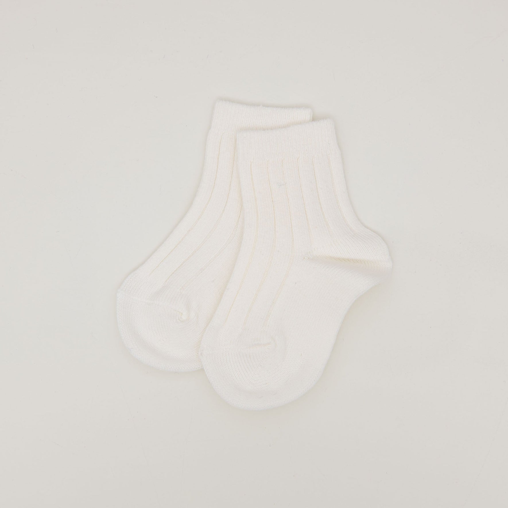 The Ribbed Socks, made from a soft cotton blend and featuring a minimalist ribbed pattern, are displayed flat on a simple, light-colored background with the heel and toe areas slightly visible.