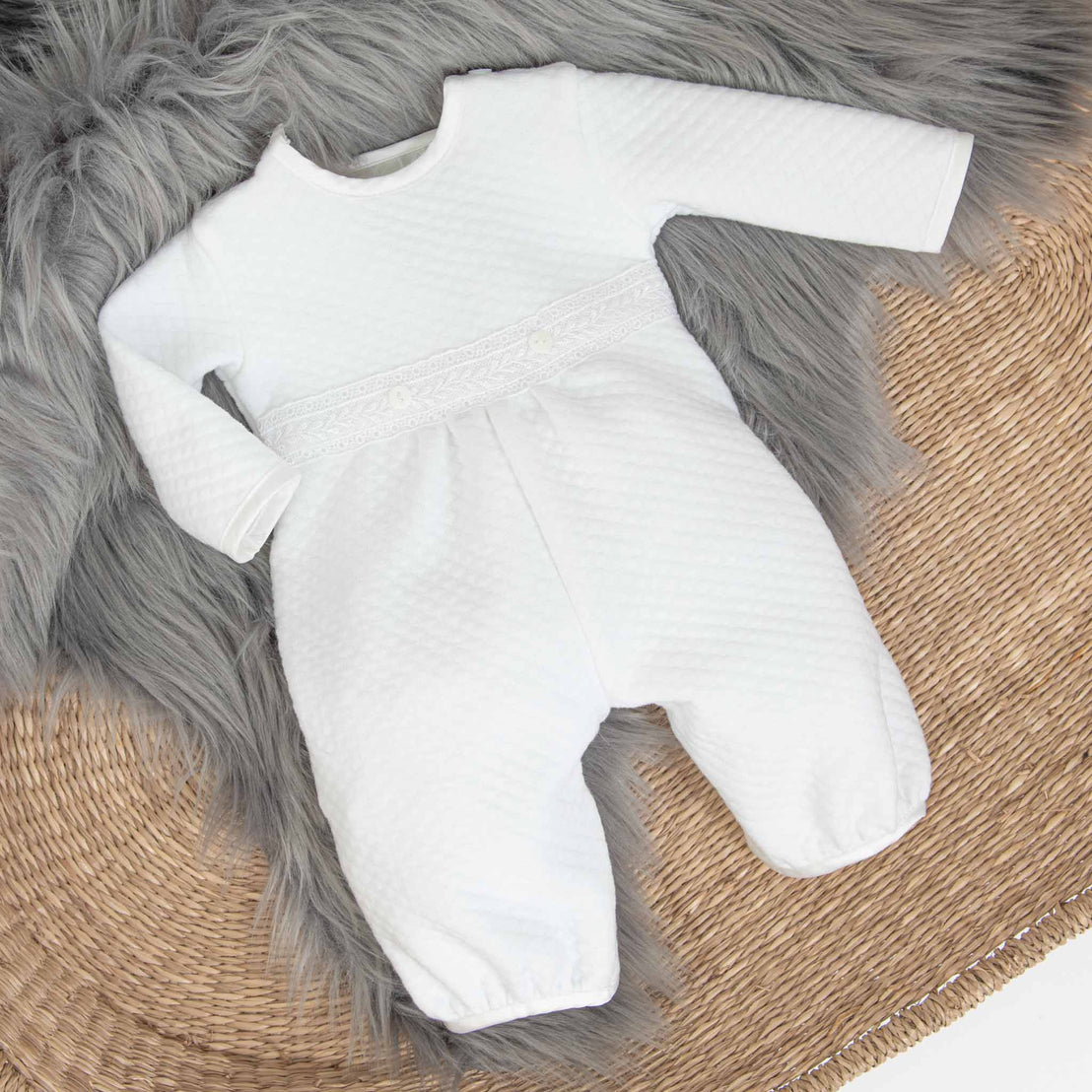 Flat lay photo of the Elijah Newborn Baby Romper laying in a cradle with a grey fur blanket