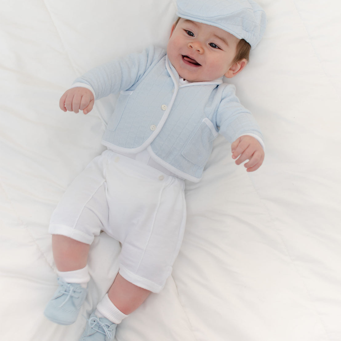 Baby boy laying on the ground and wearing the Logan 3-Piece Shorts Suit (and matching Logan Newsboy Cap).