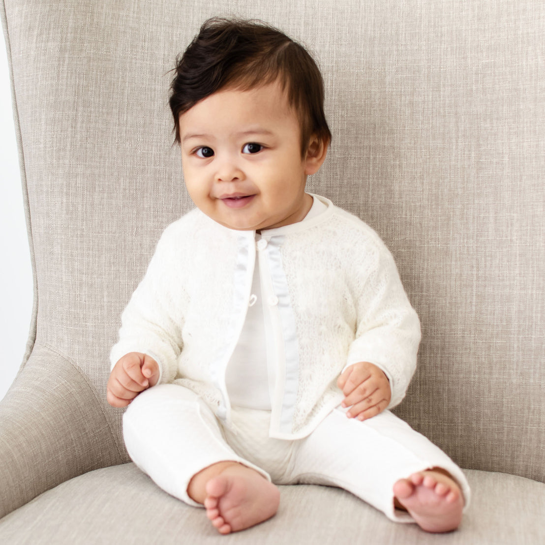 Baby boy sitting on a chair and wearing the Owen 3-Piece Suit, including the sweater, pants, and onesie