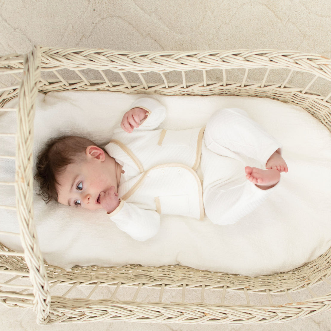 Baby laying in a cradle. He is wearing the Liam 3-Piece Suit made from a soft ivory quilted cotton and a champagne silk trim.