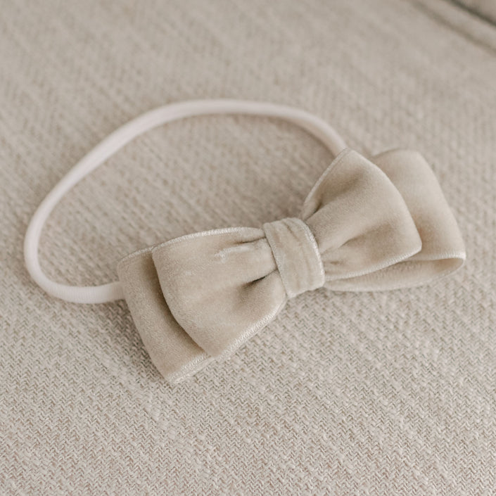 The Kristina Velvet Bow Headband, handmade in the USA, rests gracefully on a textured beige fabric surface.