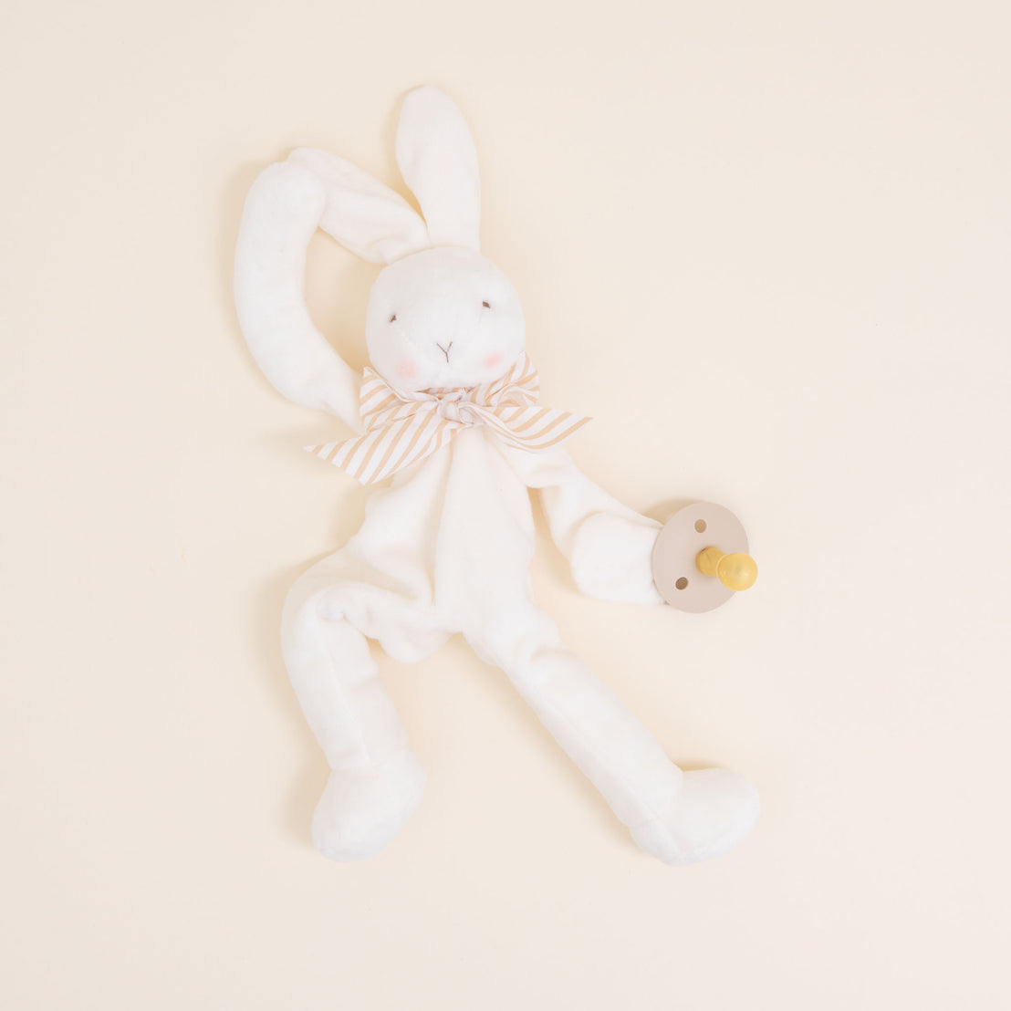 Flat lay photo of the tan Theodore Bunny Buddy Pacifier Holder. Stuffed animal floppy bunny made from a soft velour