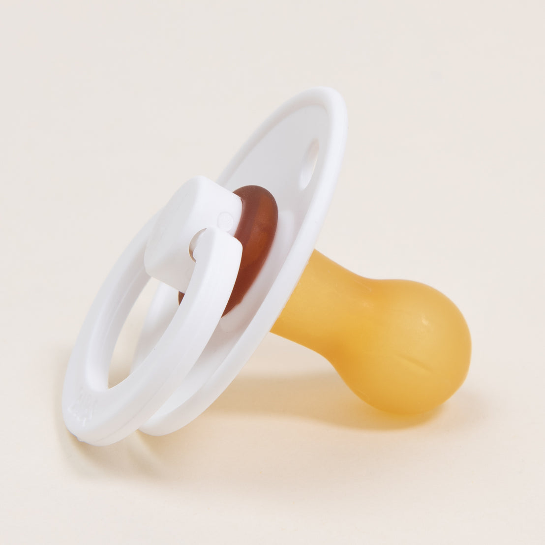 The Bibs Pacifier 2 Pack features a natural rubber nipple and white plastic shield, exuding a classic appearance. Its design includes a circular white ring attached to the shield, ideal for promoting self-soothing in little ones against its plain backdrop.