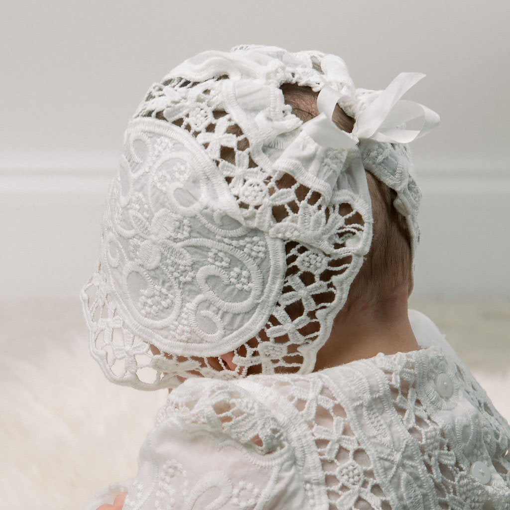 Close-up backside view of the Adeline Lace Christening Bonnet as worn by a baby girl. This angle showcases the cinched silk ribbon tie, ensuring a snug fit for the bonnet.