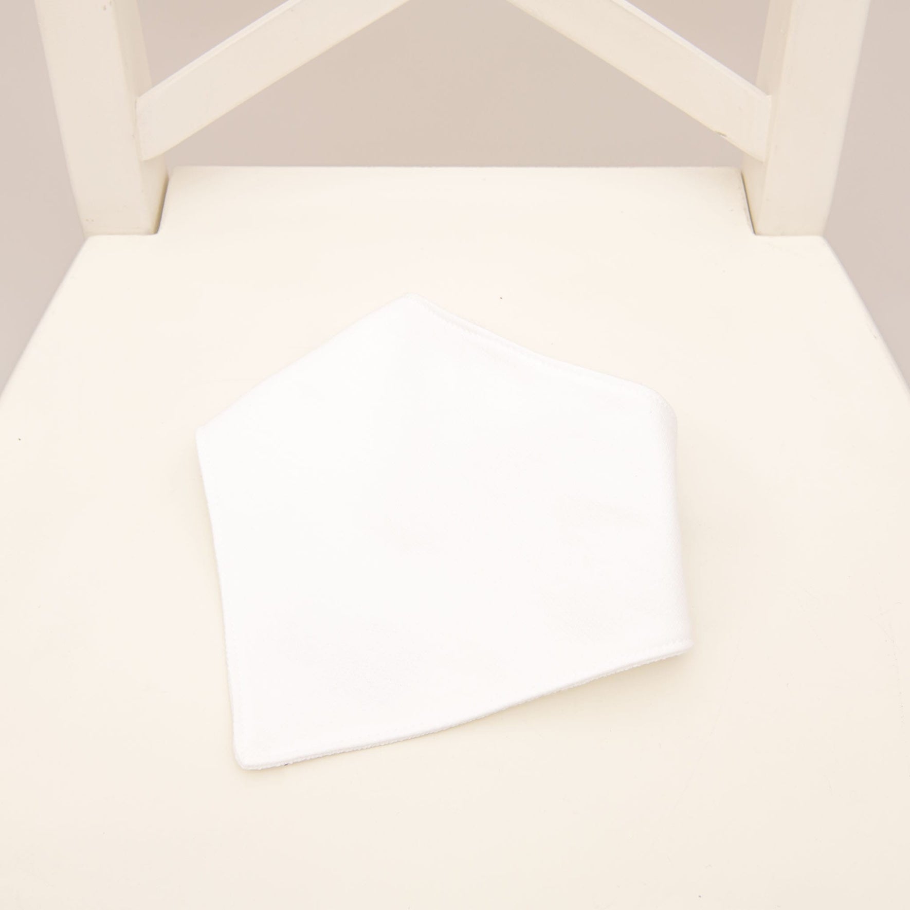 Flat lay photo of the Asher Bandana Bib made from a white French Terry cotton with button closure.