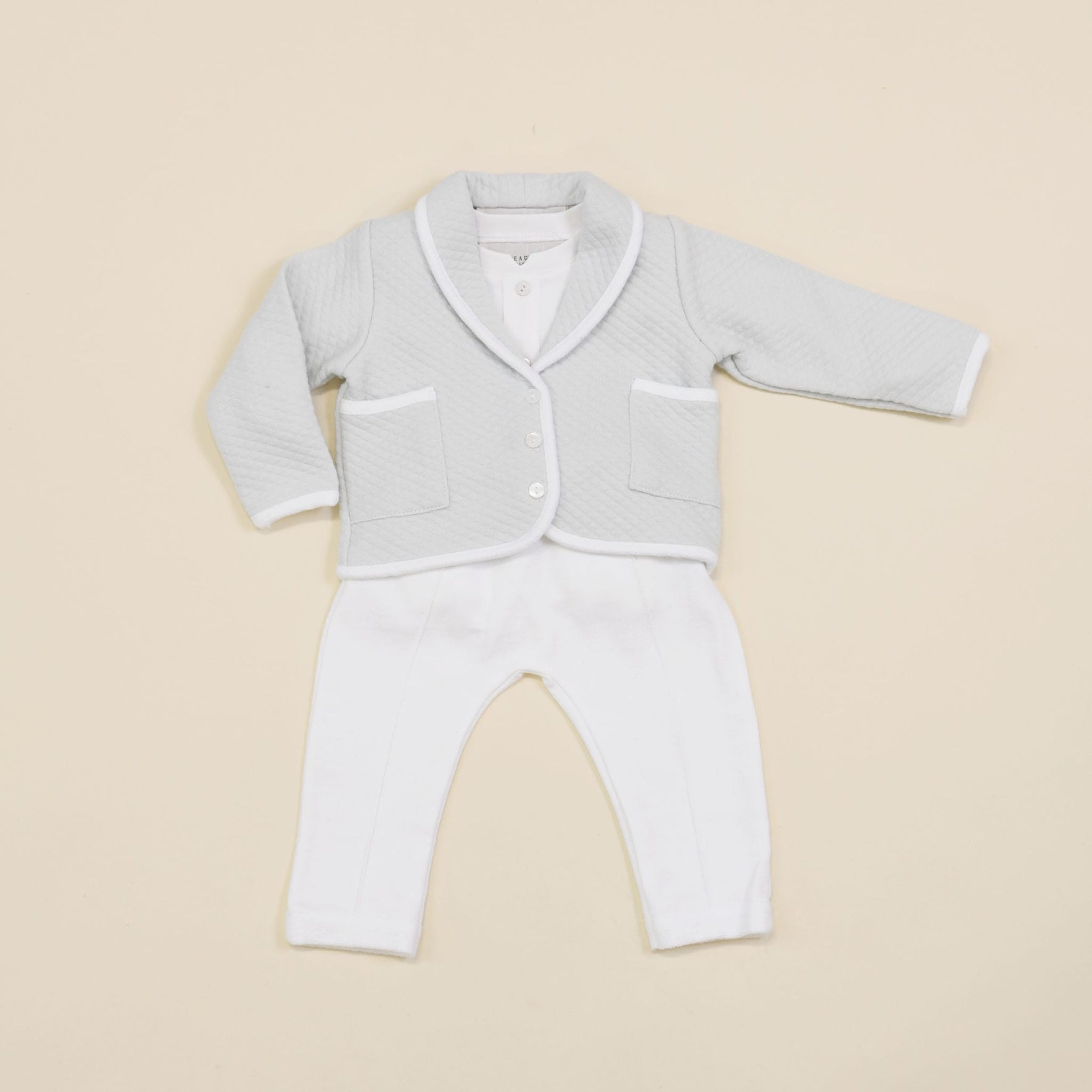 A newborn outfit with a light gray quilted cotton jacket accented by white trim and buttons, complemented by crisp white pants. This delightful ensemble, similar in style to the Asher Soft Teal 3-Piece Suit, is elegantly presented on a neutral background.