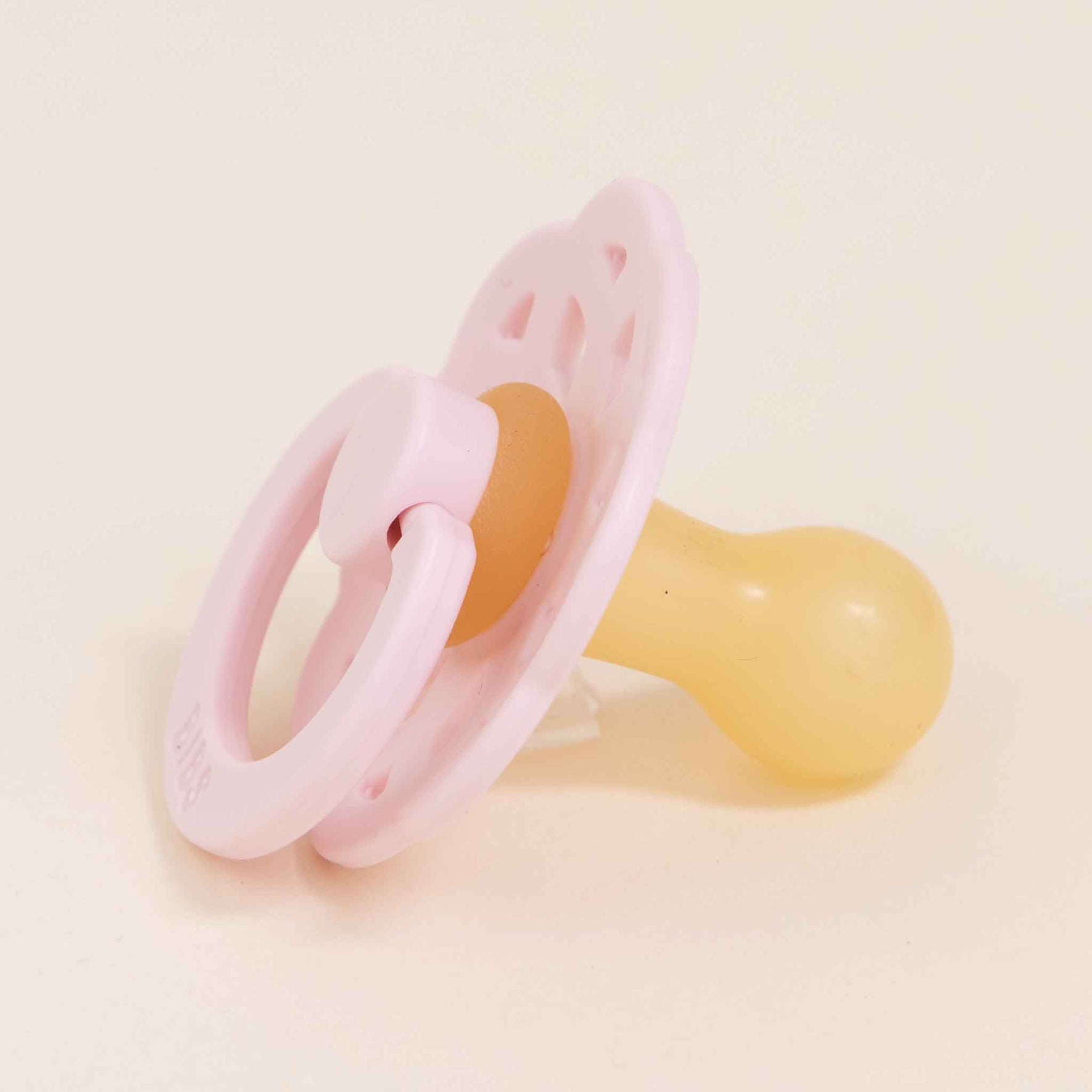 A Bibs Lace Pacifier in Blossom, part of a 2-pack set from Denmark, featuring a pink plastic ring and a yellow natural rubber nipple, rests on a light surface, showcasing its bohemian-inspired design.