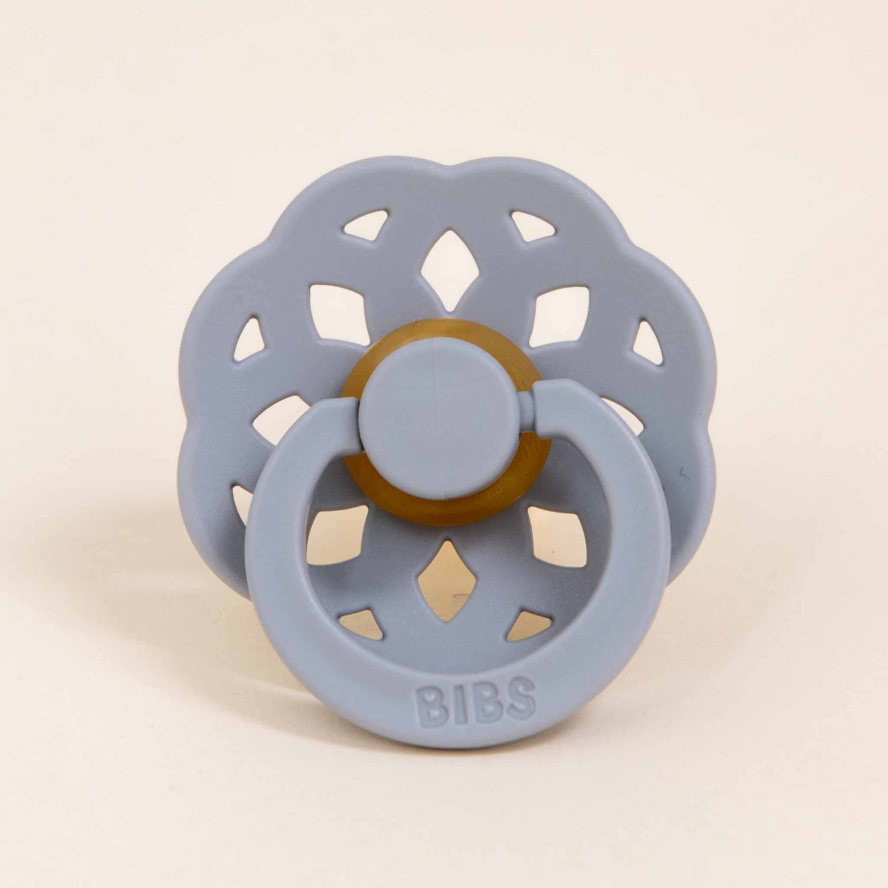 The Bibs Lace Pacifier in the color "Cloud" is positioned upright, showcasing its flower-shaped design. It includes a circular mouthpiece made from natural rubber and a decorative handle with cut-out petal shapes. Made in Denmark, the word "BIBS" is embossed on the bottom of the handle, encouraging your baby to naturally self-soothe.