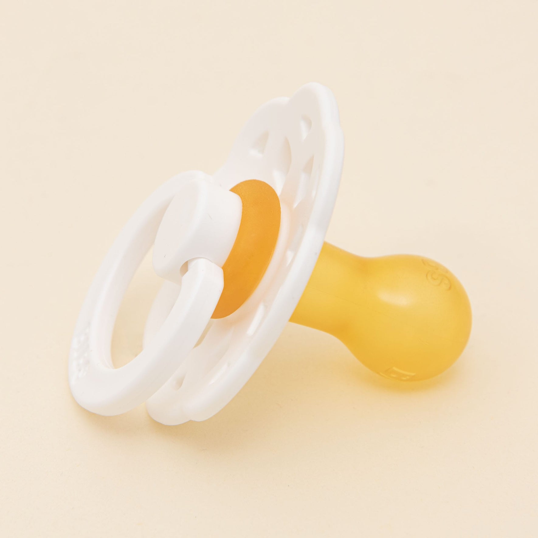 A Bibs Lace Pacifier in yellow with a white handle and decorative ring, made from natural rubber for a bohemian-inspired design, is placed on a neutral light background.