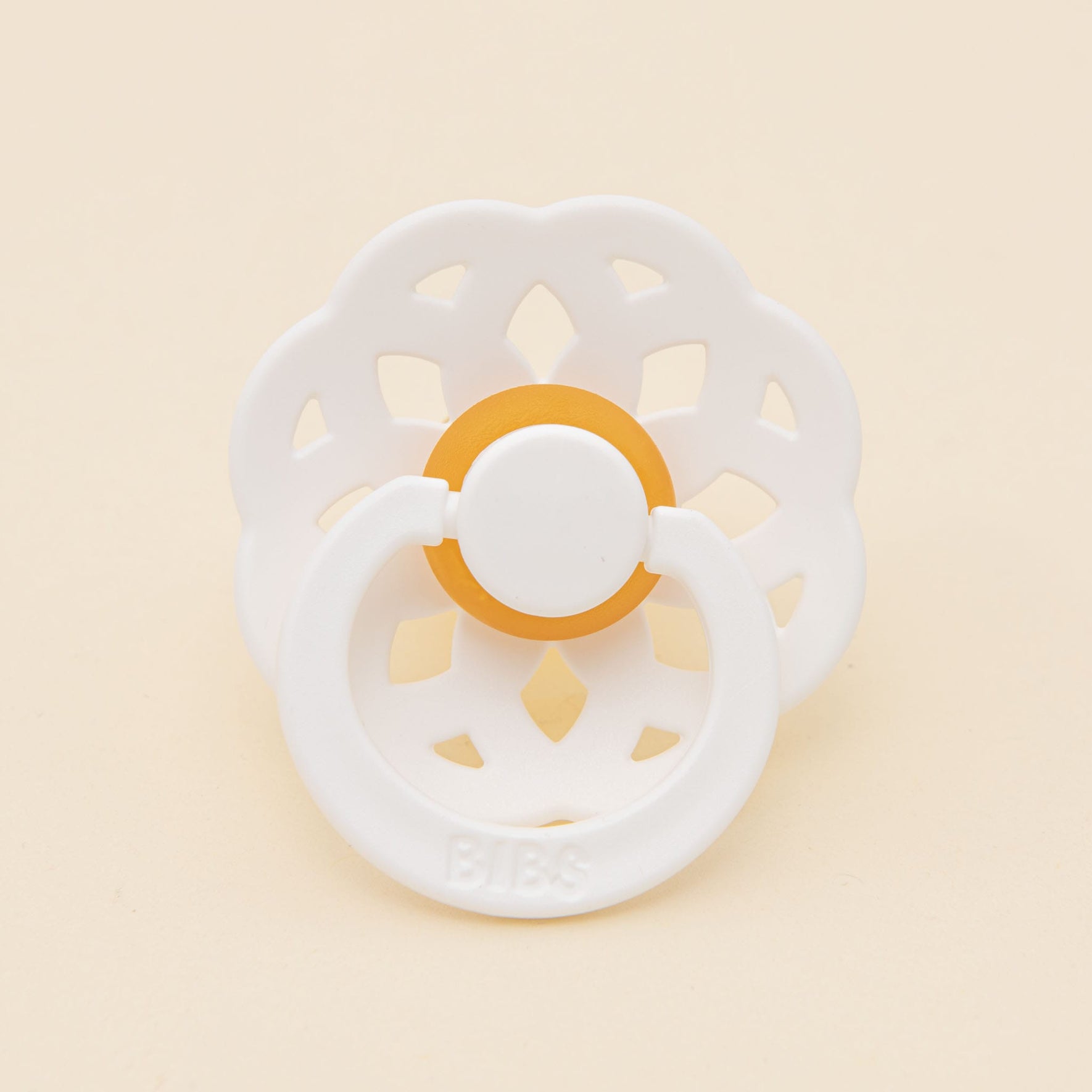 The Bibs Lace Pacifier from the 2-pack in White showcases a bohemian-inspired design with a floral-patterned shield and an orange accent, set against a plain, light background.