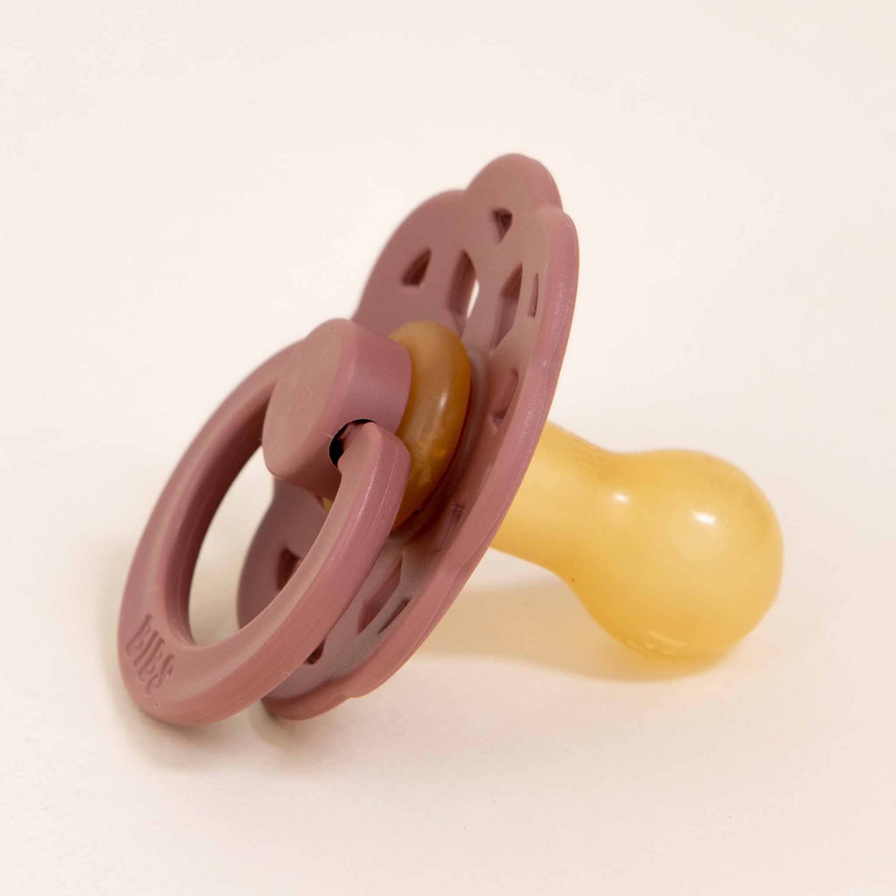 A Bibs Lace Pacifier from the Woodchuck set, made from natural rubber in pink and yellow hues, showcases a round handle and vented shield against a neutral backdrop. This delightful accessory merges practicality with the self-soothing comfort that babies adore.