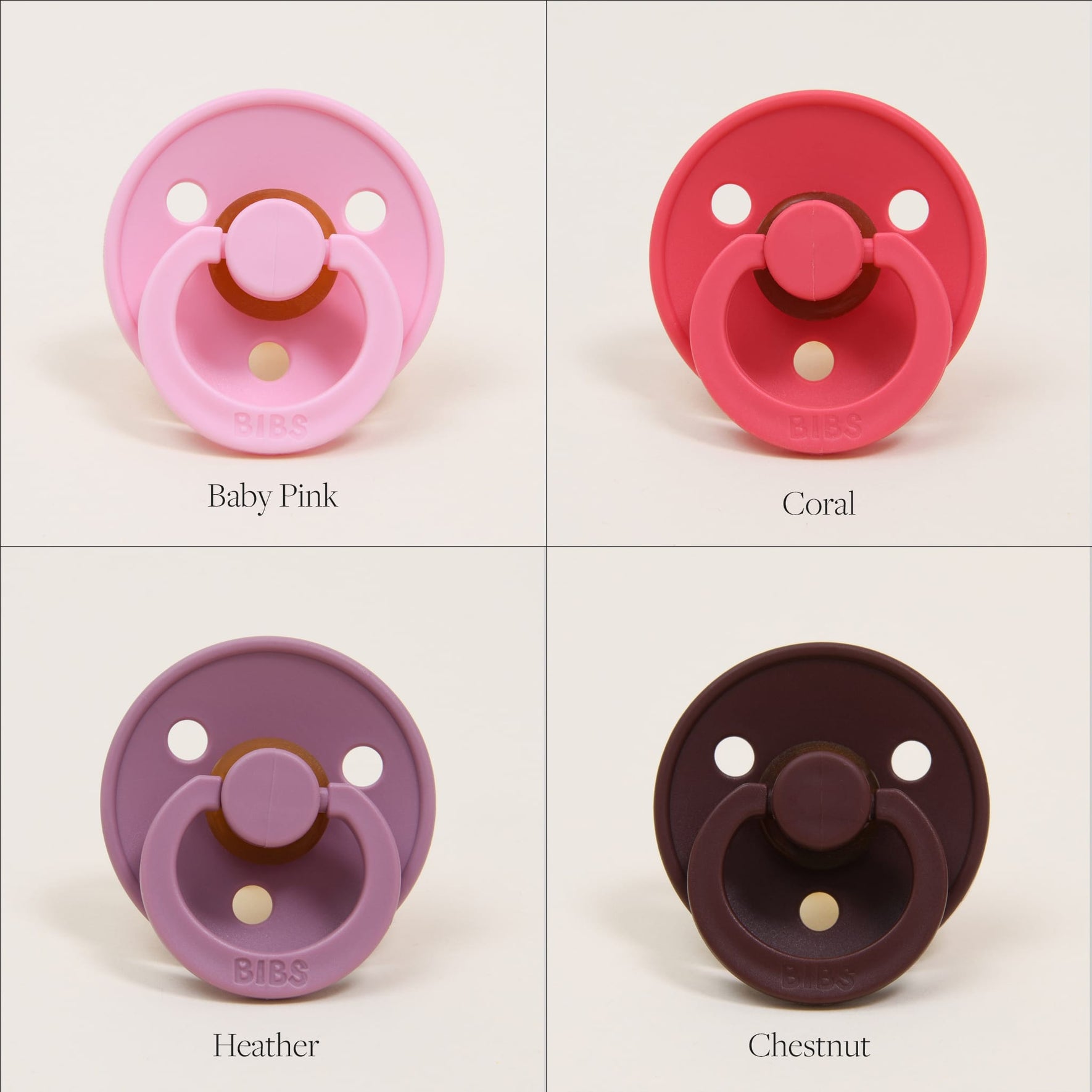 A set of four Bibs Pacifiers made from natural rubber are displayed in a grid formation against a white background. The top left is baby pink, the top right coral, the bottom left heather, and the bottom right chestnut. These pacifiers are crafted in Denmark and each includes two vent holes along with a circular handle to assist with self-soothing moments.