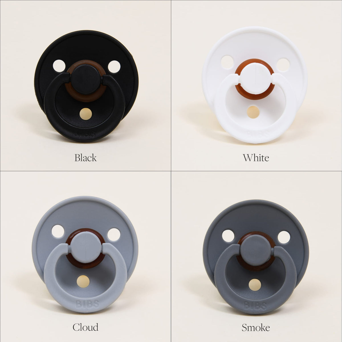Four Bibs Pacifiers are displayed, each made from natural rubber to ensure comfort and safety. The top left pacifier is black, the top right is white, the bottom left features a light gray shade labeled "Cloud," and the bottom right showcases a darker gray hue labeled "Smoke." These pacifiers, manufactured in Denmark, are designed to help babies self-soothe with ease.