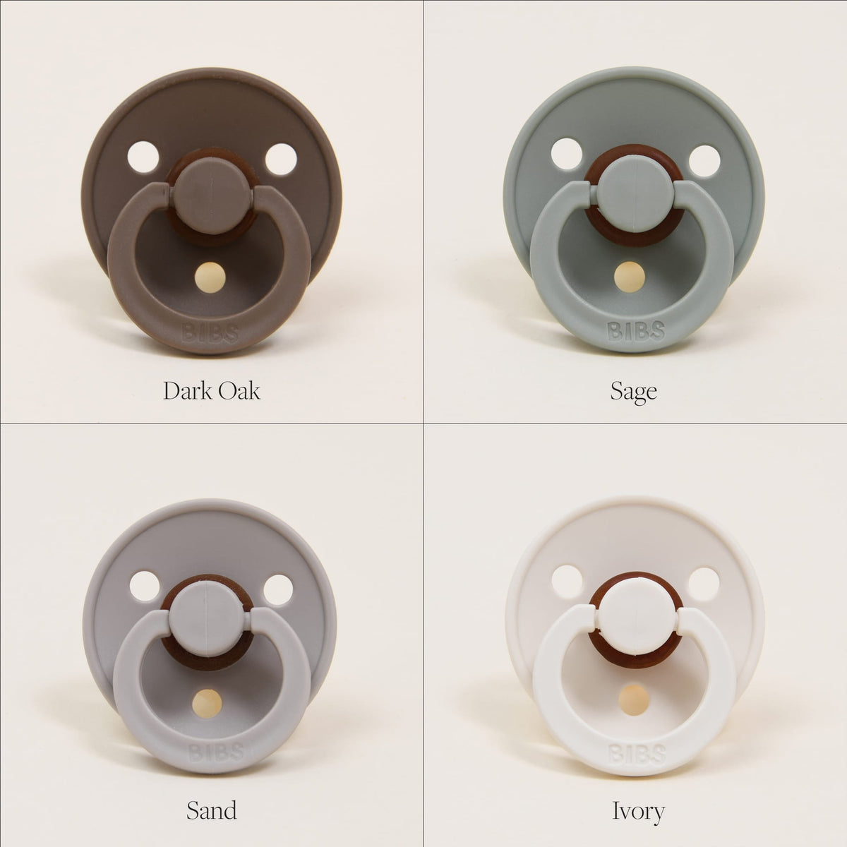 Displayed in a grid, four Bibs Pacifiers made from natural rubber offer a gentle touch. The "Dark Oak" pacifier in brown is positioned at the top left, "Sage" in green at the top right, "Sand" in beige at the bottom left, and "Ivory" in white at the bottom right. These pacifiers are crafted with round shields and ring handles to promote self-soothing and are manufactured in Denmark.
