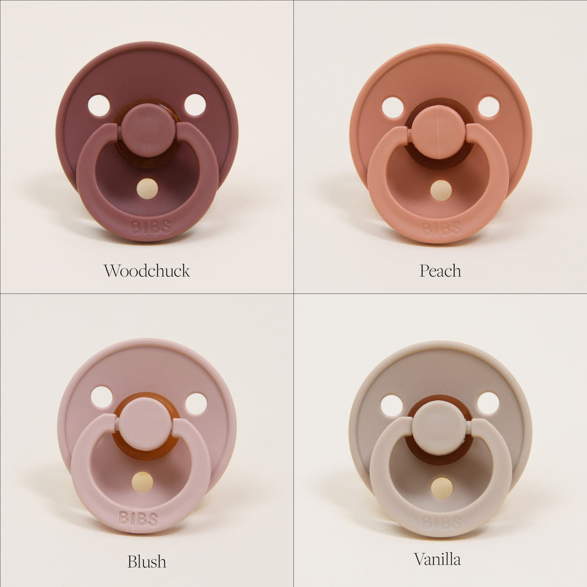 A set of four Bibs Pacifiers displayed in a grid showcases a variety of vibrant colors. The top left features "Woodchuck" in dark mauve, the top right is "Peach" in light orange, the bottom left presents "Blush" in soft pink, and the bottom right displays "Vanilla" in light cream. These pacifiers are crafted from natural rubber by BIBS, Denmark.