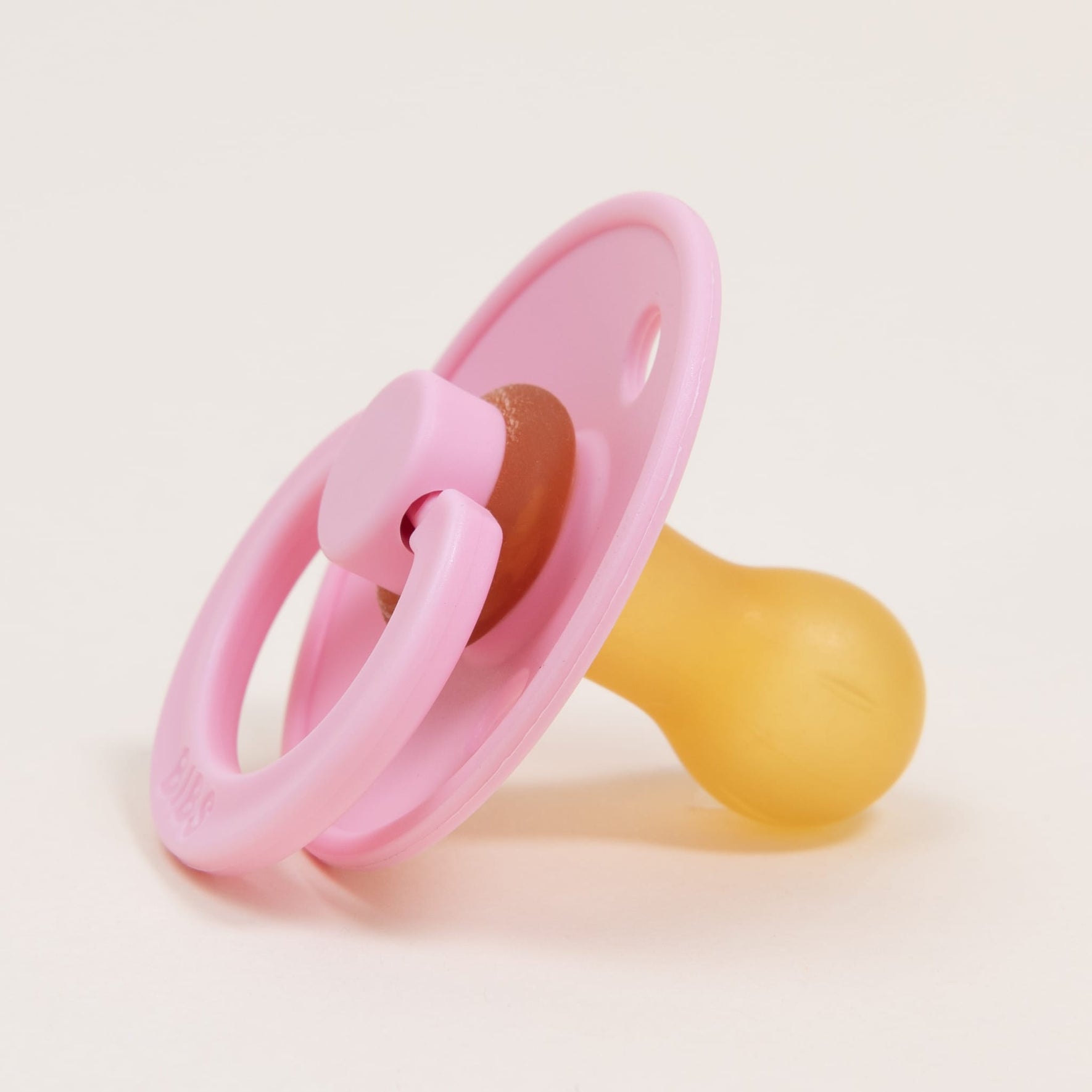 A Bibs Pacifier in Baby Pink, featuring a classic design with a round silicone nipple and circular handle attached to the plastic shield, is displayed on a white background, perfect for helping babies self-soothe effectively.