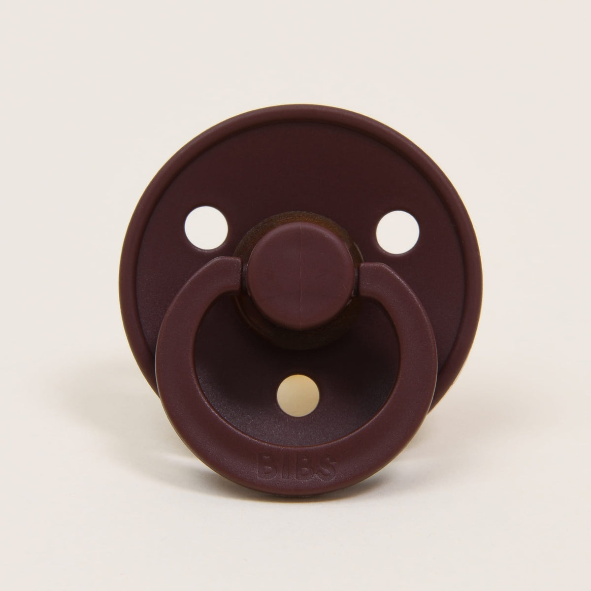 The Bibs Pacifier 2 Pack in Chestnut from Denmark showcases a dark brown natural rubber pacifier featuring a round shield with two small ventilation holes. The circular handle and embossed "BIBS" brand name are positioned at the bottom, crafted to aid babies in self-soothing. It is elegantly centered against a plain background.