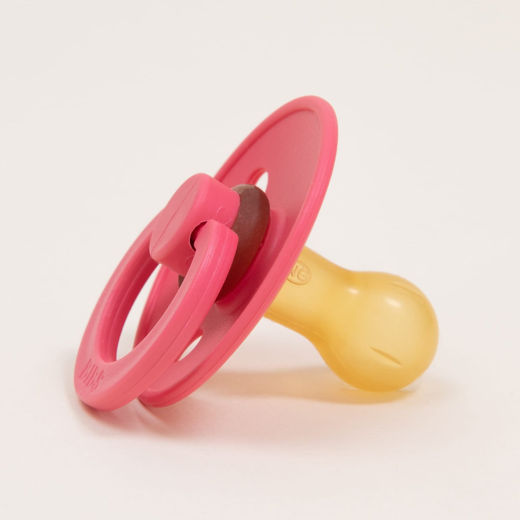 A Bibs Pacifier from the 2-pack Coral collection is showcased against a plain white background. Made in Denmark, this pacifier features a pink and yellow natural rubber design with a rounded silicone nipple and a circular plastic shield equipped with a handle, perfect for helping infants self-soothe.