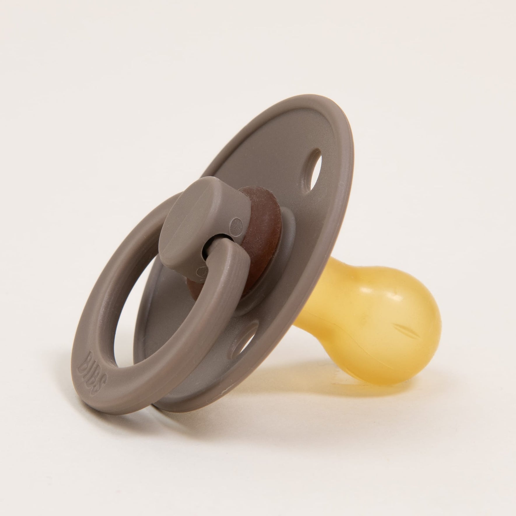 The Bibs Pacifier 2 Pack in Dark Oak showcases a timeless design with its natural rubber nipple and circular shield, complete with two ventilation holes. Ideal for self-soothing, it rests elegantly at a slight angle against a neutral backdrop.