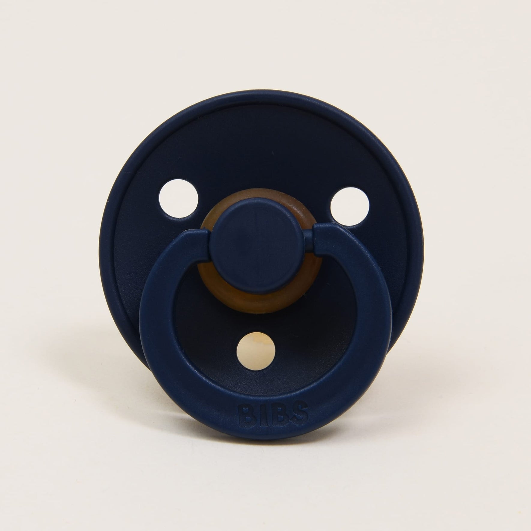 The Bibs Pacifier 2 Pack in "Deep Space" features a natural rubber pacifier with a dark blue round shield, complete with three ventilation holes and a convenient ring handle. Designed and crafted in Denmark, this pacifier aids babies in self-soothing while shown against a simple, light backdrop.
