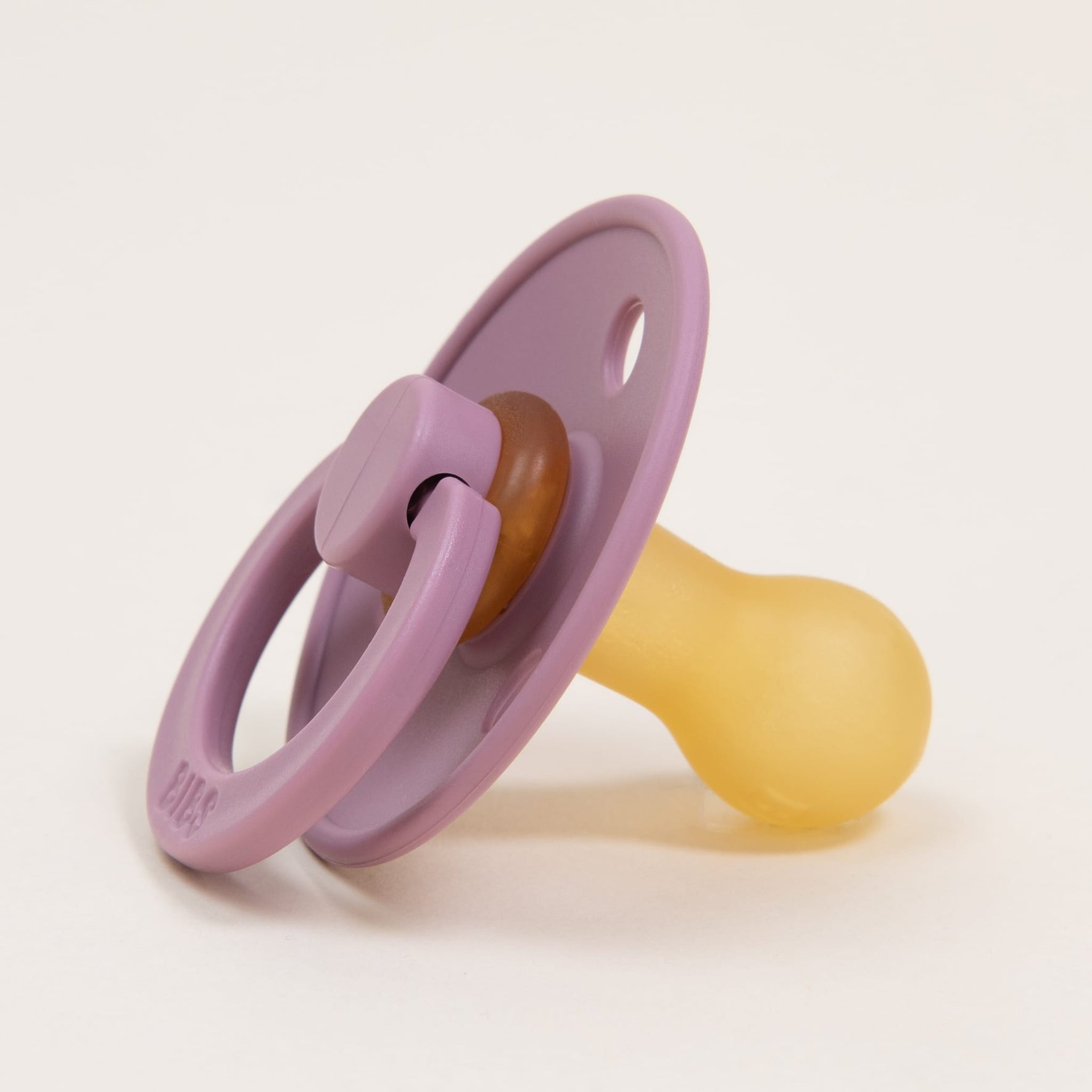 A timeless and elegant Bibs Pacifier in soft heather, with a natural rubber nipple, rests on a neutral, off-white background. The minimalist design is accentuated by its circular handle—perfect for helping your baby self-soothe.