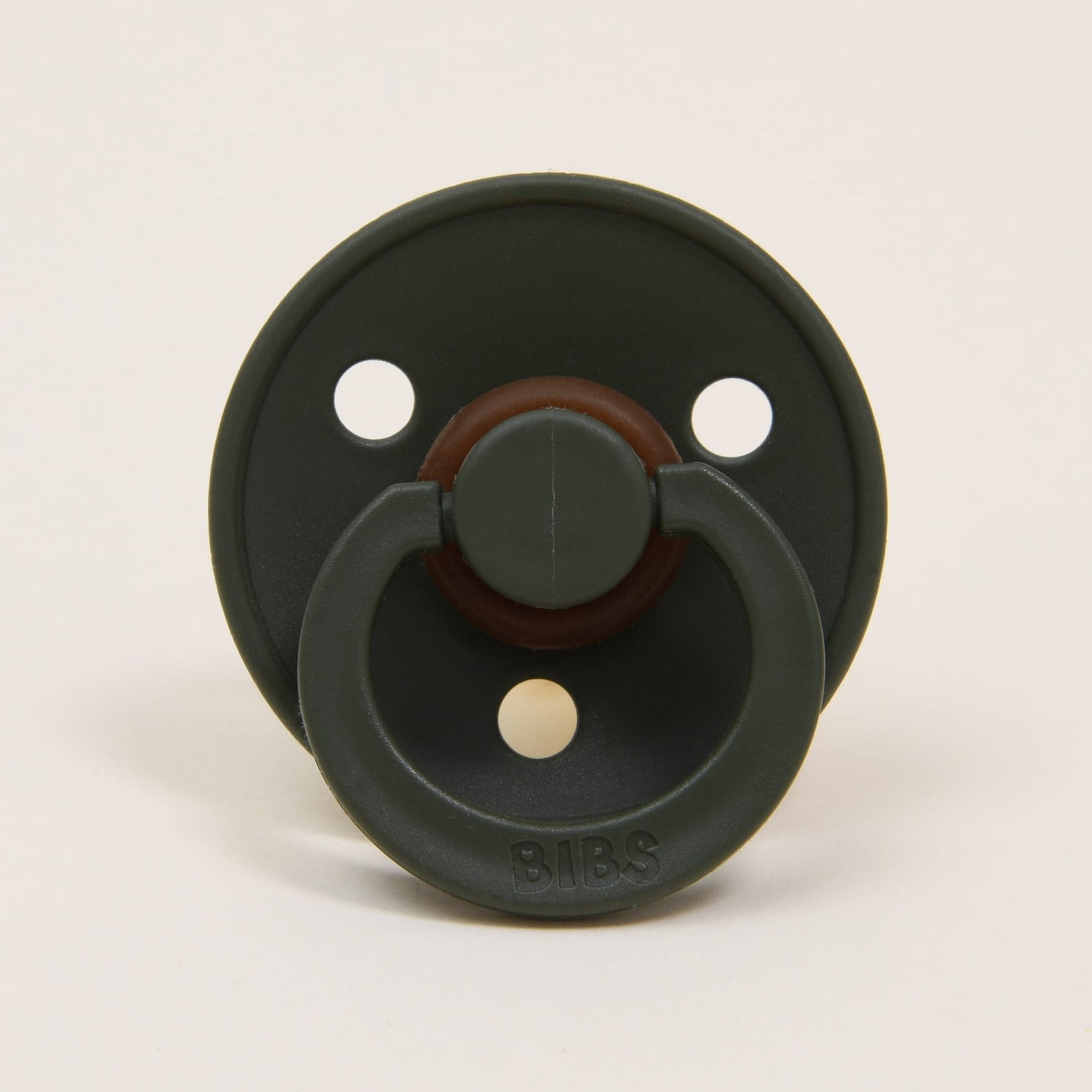 A pacifier from the Bibs Pacifier 2 Pack | Hunter collection showcases a classic design with a green hue, featuring three ventilation holes on the shield and a brown accent around its natural rubber nipple base, set against a simple light background. The brand name "BIBS" is embossed on the front, providing babies with an elegant option for self-soothing.