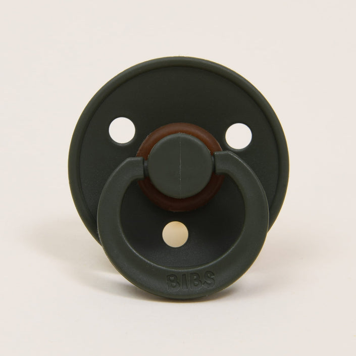 A pacifier from the Bibs Pacifier 2 Pack | Hunter collection showcases a classic design with a green hue, featuring three ventilation holes on the shield and a brown accent around its natural rubber nipple base, set against a simple light background. The brand name "BIBS" is embossed on the front, providing babies with an elegant option for self-soothing.