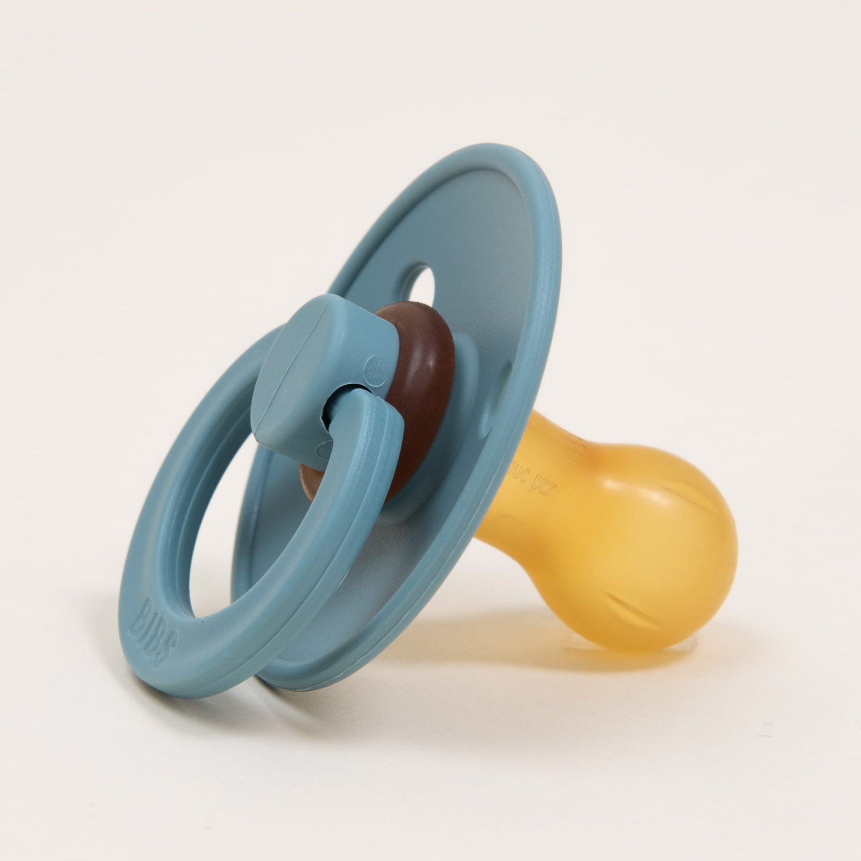A Bibs Pacifier from the Island Sea 2 Pack, crafted from natural rubber in soothing blue and yellow hues with a rounded yellow nipple, complemented by a blue circular shield and ring handle, designed and manufactured in Denmark, rests serenely on a plain white background.