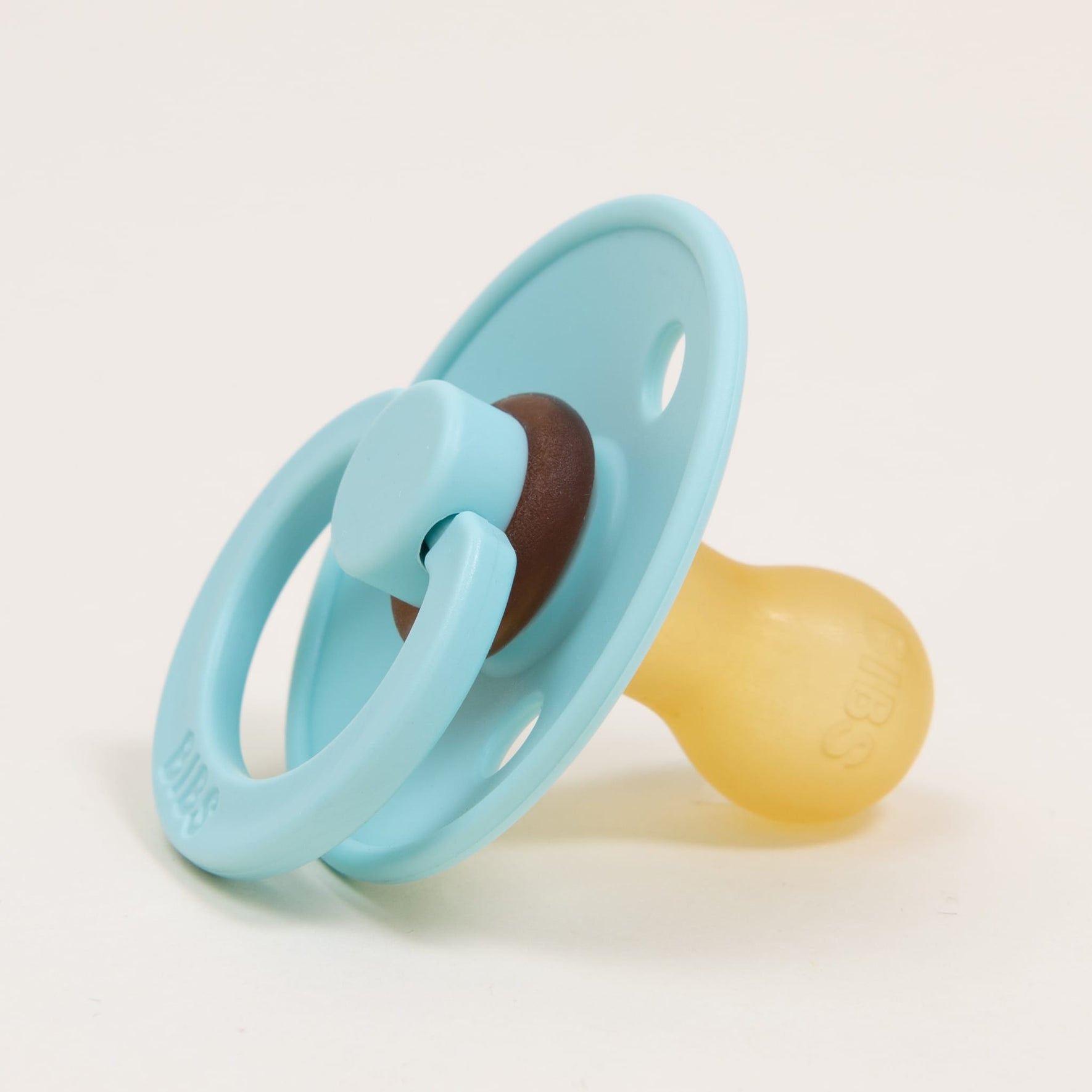 A mint pacifier featuring a brown center and a beige natural rubber nipple is placed on a white background. Designed and manufactured in Denmark, the Bibs Pacifier 2 Pack encourages babies to self-soothe effortlessly.