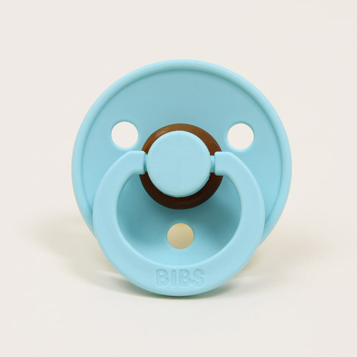 A mint pacifier with a circular shield featuring two holes, crafted from natural rubber to aid in soothing babies. The handle is embossed with the brand name "Bibs," which is renowned for its design and manufacturing in Denmark.