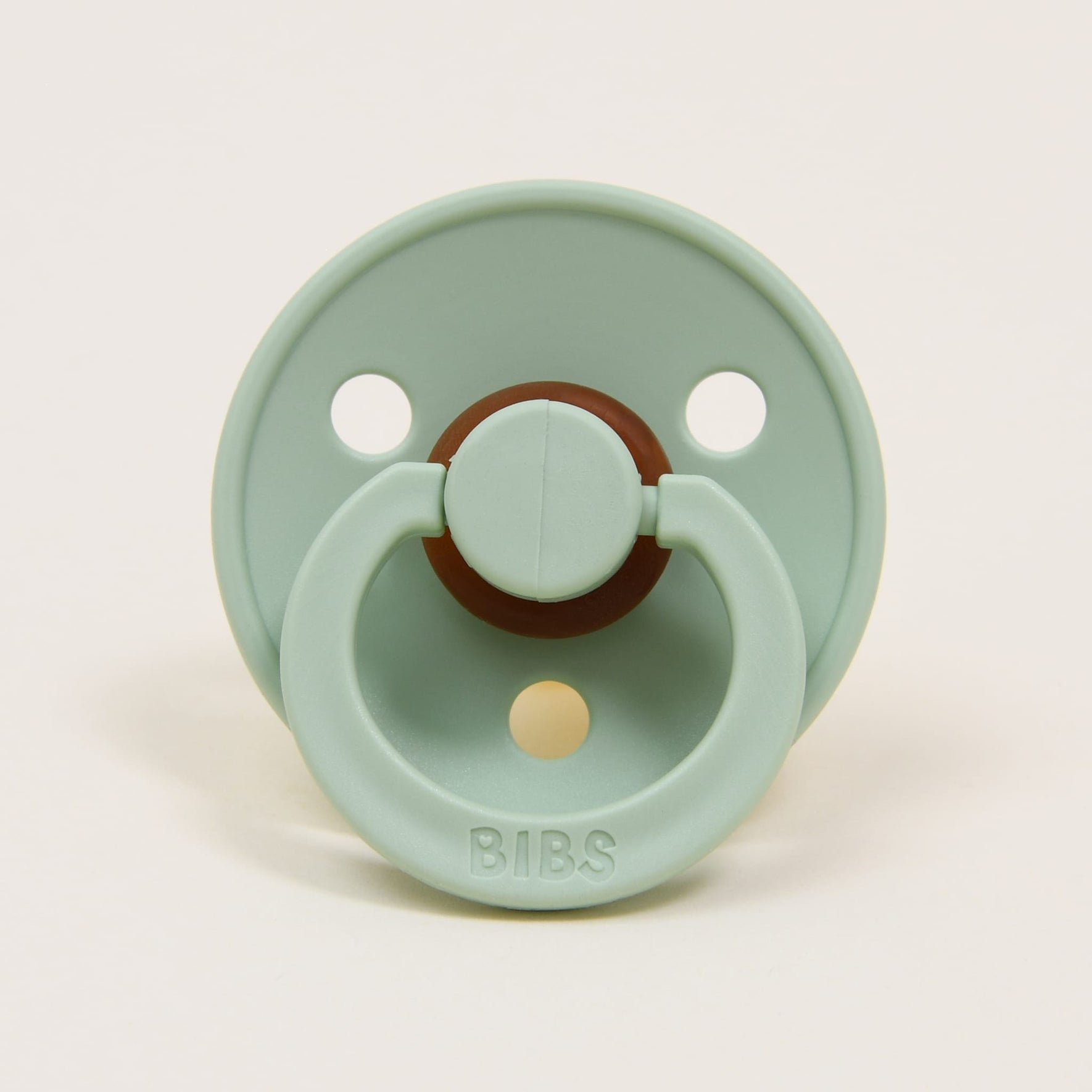 A pistachio-colored natural rubber baby pacifier with a round shield and an attached ring. The brand name "Bibs" is embossed on the bottom of the shield, which features two ventilation holes. Designed in Denmark, it's perfect for helping your baby self-soothe.