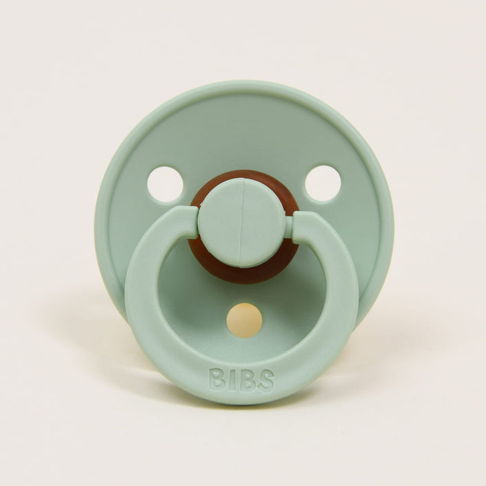 A pistachio-colored natural rubber baby pacifier with a round shield and an attached ring. The brand name "Bibs" is embossed on the bottom of the shield, which features two ventilation holes. Designed in Denmark, it's perfect for helping your baby self-soothe.