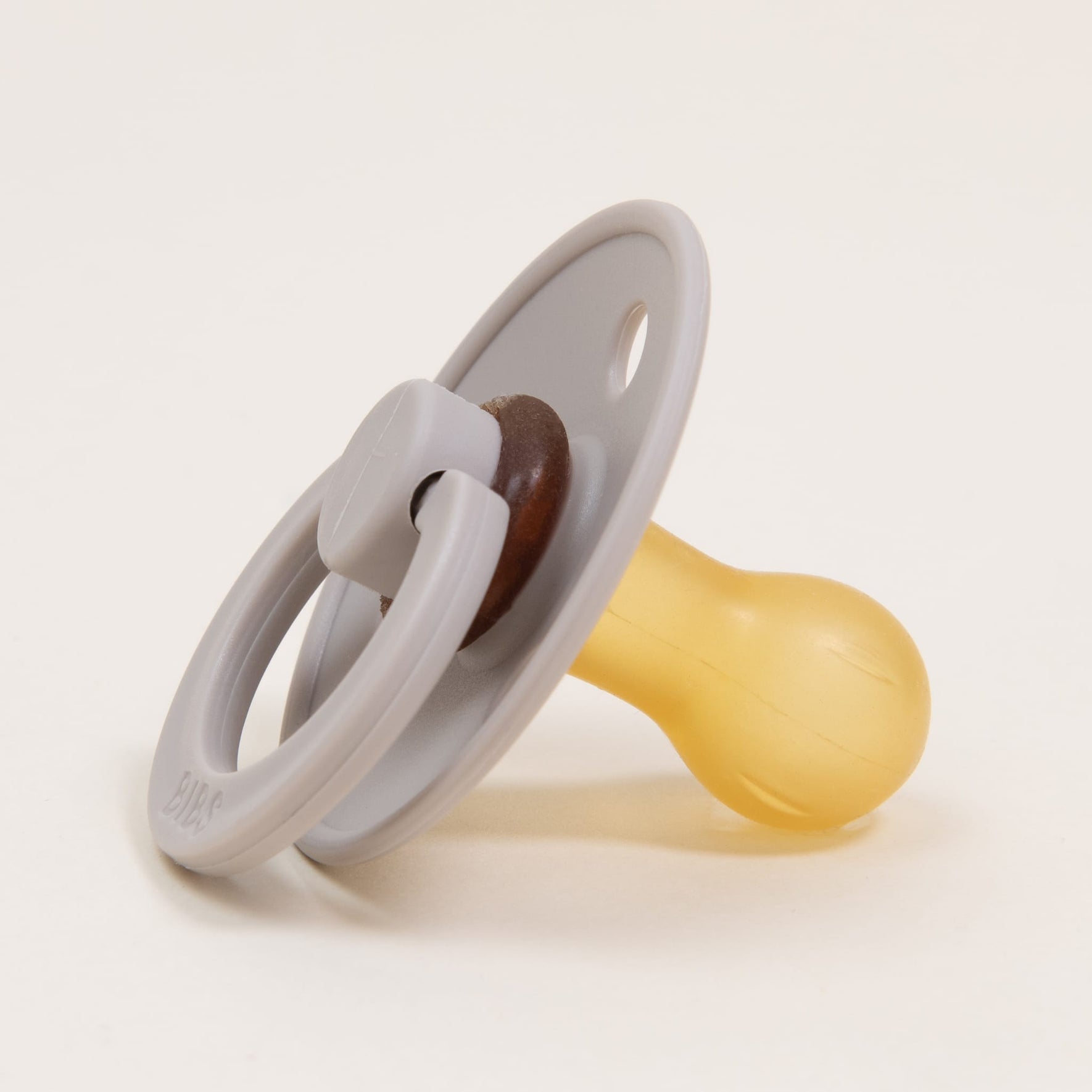 A sand-colored pacifier from the Bibs Pacifier 2 Pack features a round shield and a yellow natural rubber nipple, set against a white background. Designed for simplicity, this minimalist pacifier encourages little ones to self-soothe and embodies Denmark's renowned craftsmanship.