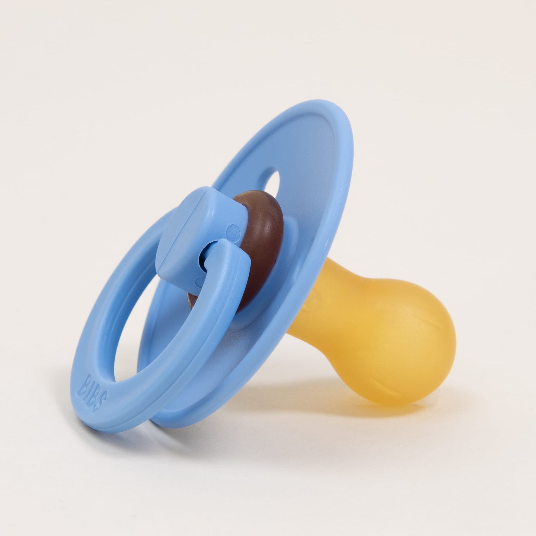 A timeless and elegant Bibs Pacifier from the Sky Blue 2 Pack, featuring a blue shield, a brown center, and a yellow nipple, is gracefully positioned on a white background, ready to help your little one self-soothe.